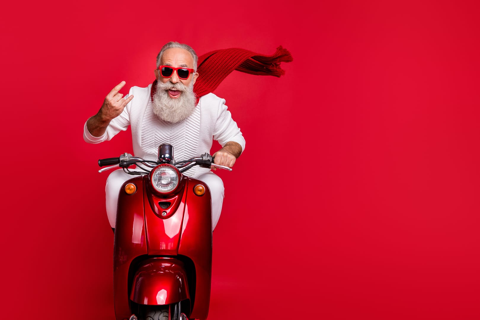Portrait of funky pensioner in eyewear eyeglasses showing rock-and-roll, sign driving bike wearing white jumper isolated over red background