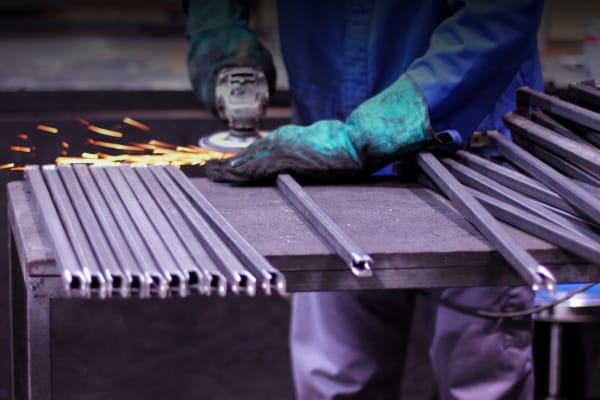 Mitarbeiter schleift Metallstangen mit dem Winkelschleifer in der Metallverarbeitung