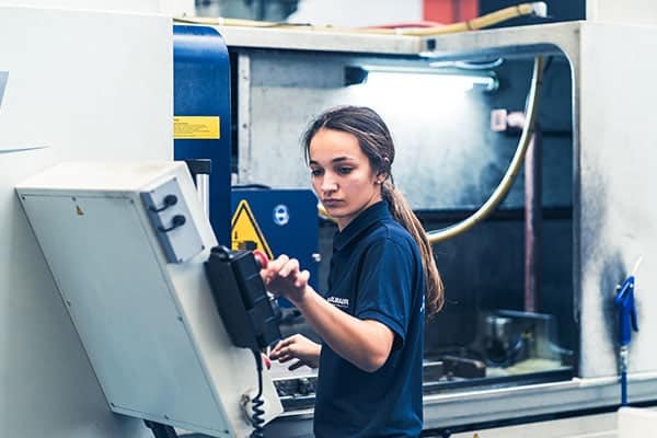 Mitarbeiterin programmiert eine CNC-Maschine für die Zerspanung am Bedienpanel