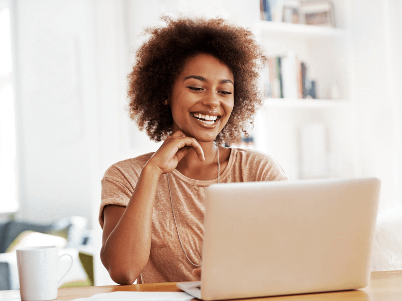 Eine junge Frau arbeitet lächelnd mit ihrem Laptop an der intuitiven Jobsuche von Meine Karriere24.